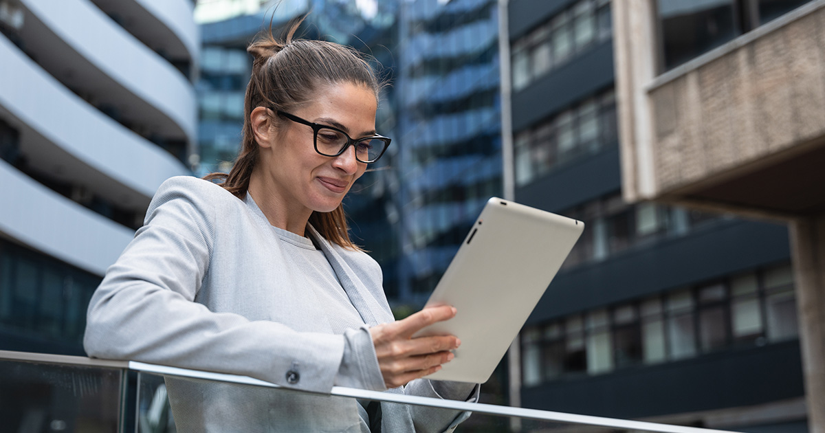 Porträt einer erfolgreichen Geschäftsfrau, die vor einem modernen Geschäftsgebäude ein digitales Tablet benutzt.
